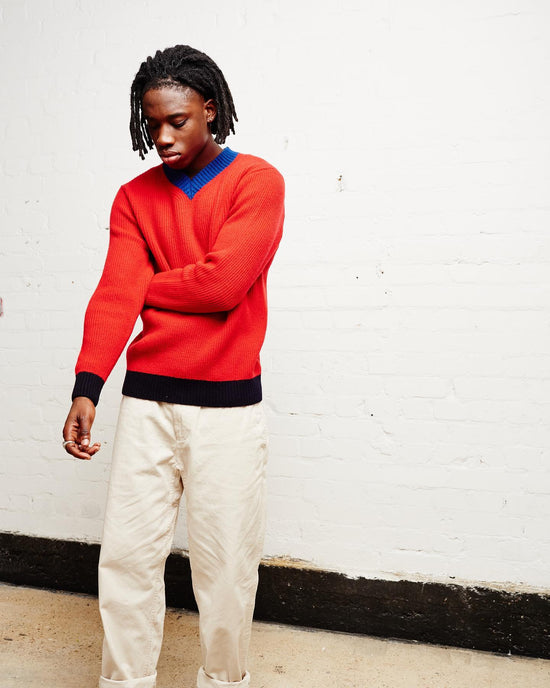 A man wears a bright red knit sweater with khaki pants. 