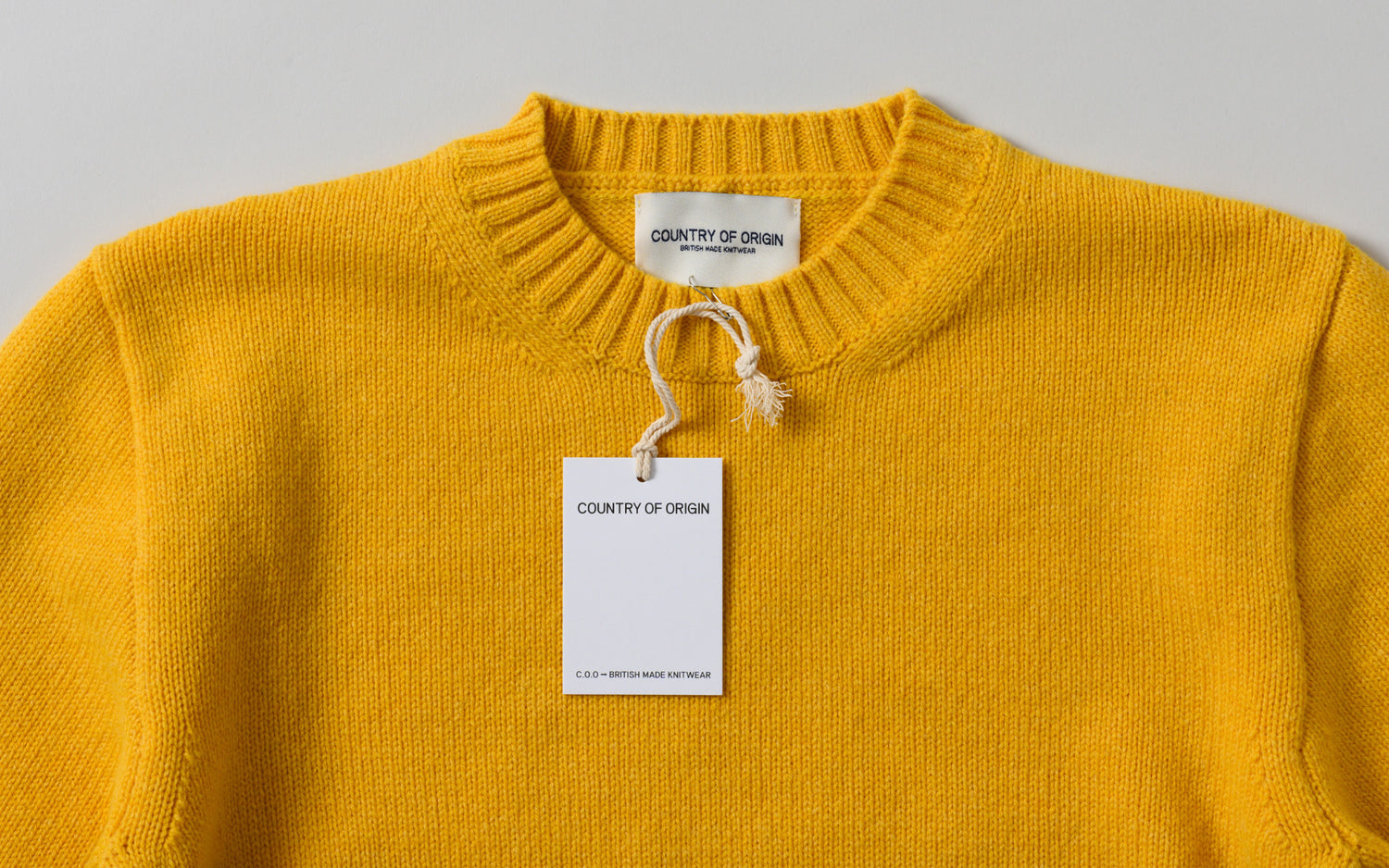 A bright yellow knit sweater, showing a country of origin hang tag. 