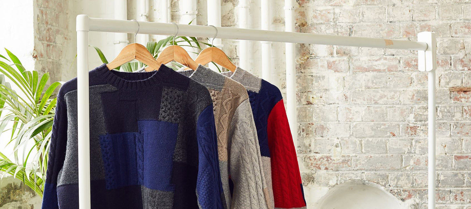 Knit sweaters hang on a rack in a bright room.